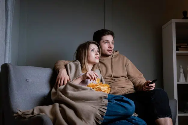 Jovem casal noite aconchegante em casa com edredon e Netflix