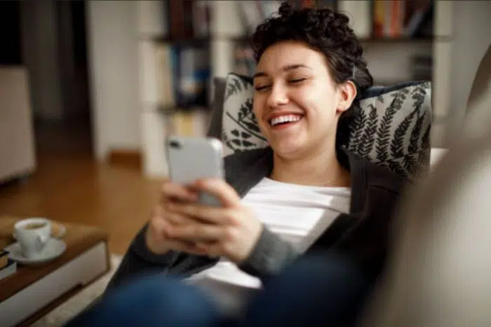 Moça sorrindo trocando mensagens com um canceriano, deitada no sofá