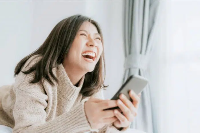 Moça dando risada com o celular na mão