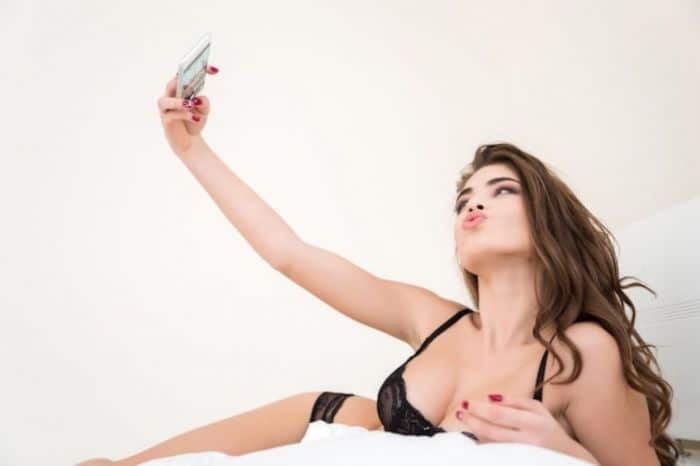 A mulher mandando uma selfie só de calcinha e sutiã para seduzir um homem na cama