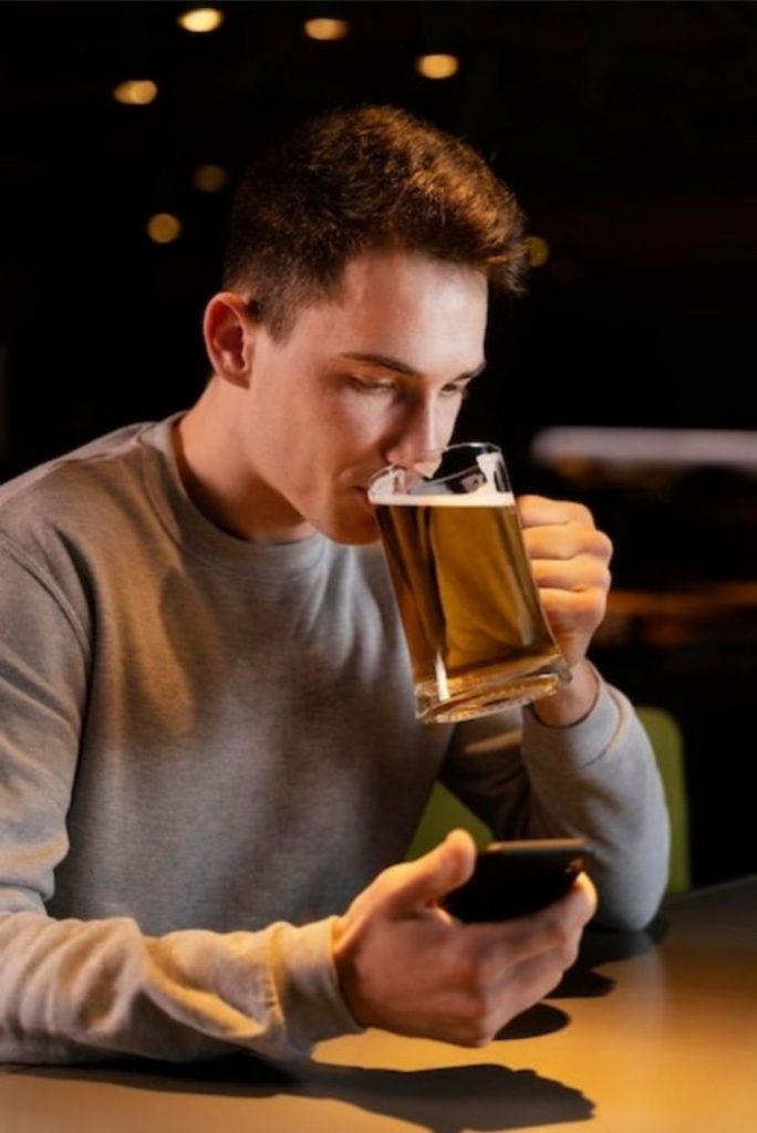 Rapaz bebendo cerveja e trocando mensagens pelo WhatsApp