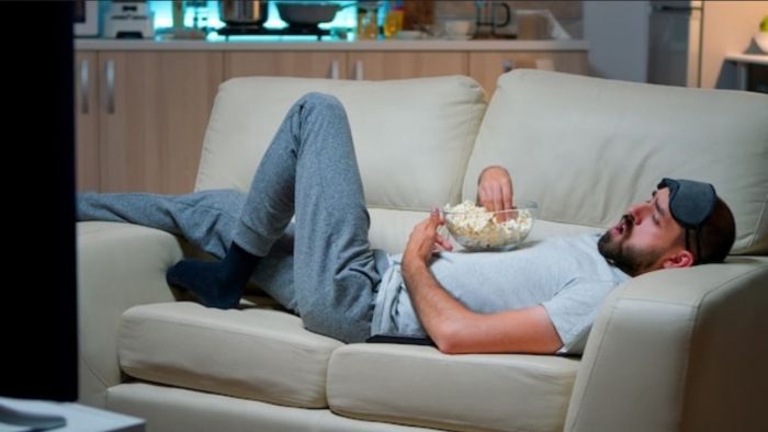 Homem deitado no sofá comendo pipoca