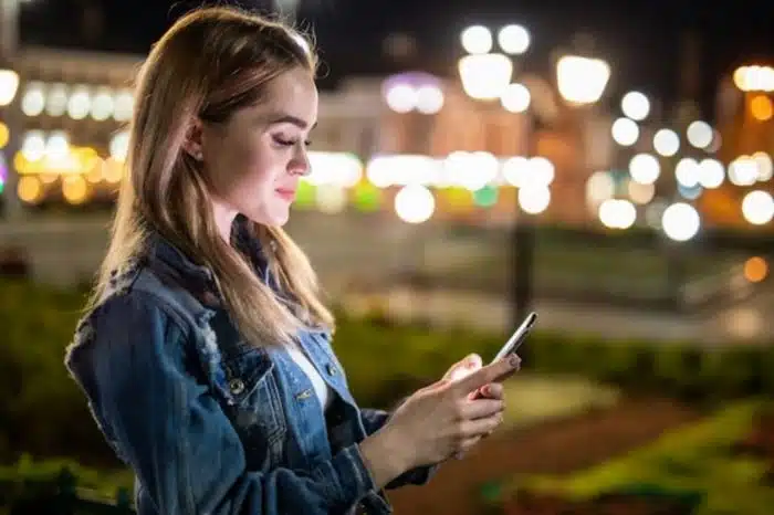 Moça com o celular na mão postando mensagens nas redes sociais