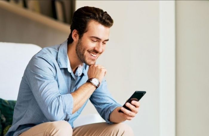 Homem sorridente com o celular na mão recebendo mensagem
